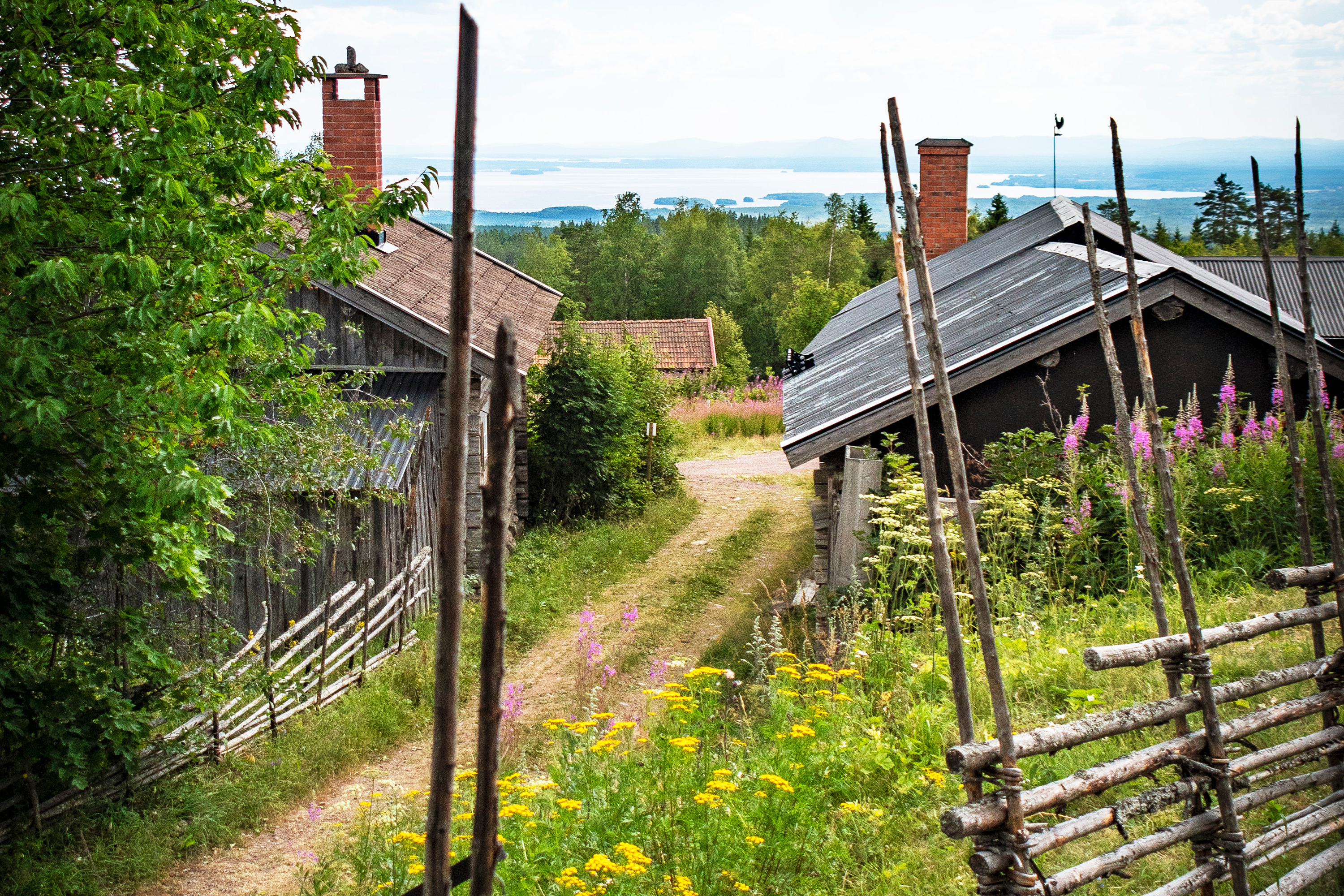 gärdsgård och fäbod i förgrunden med utsikt över sjö och skog,