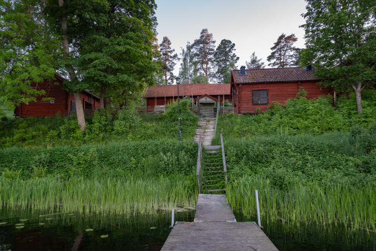Faluröd gårdslänga omgiven av grönska sommartid.