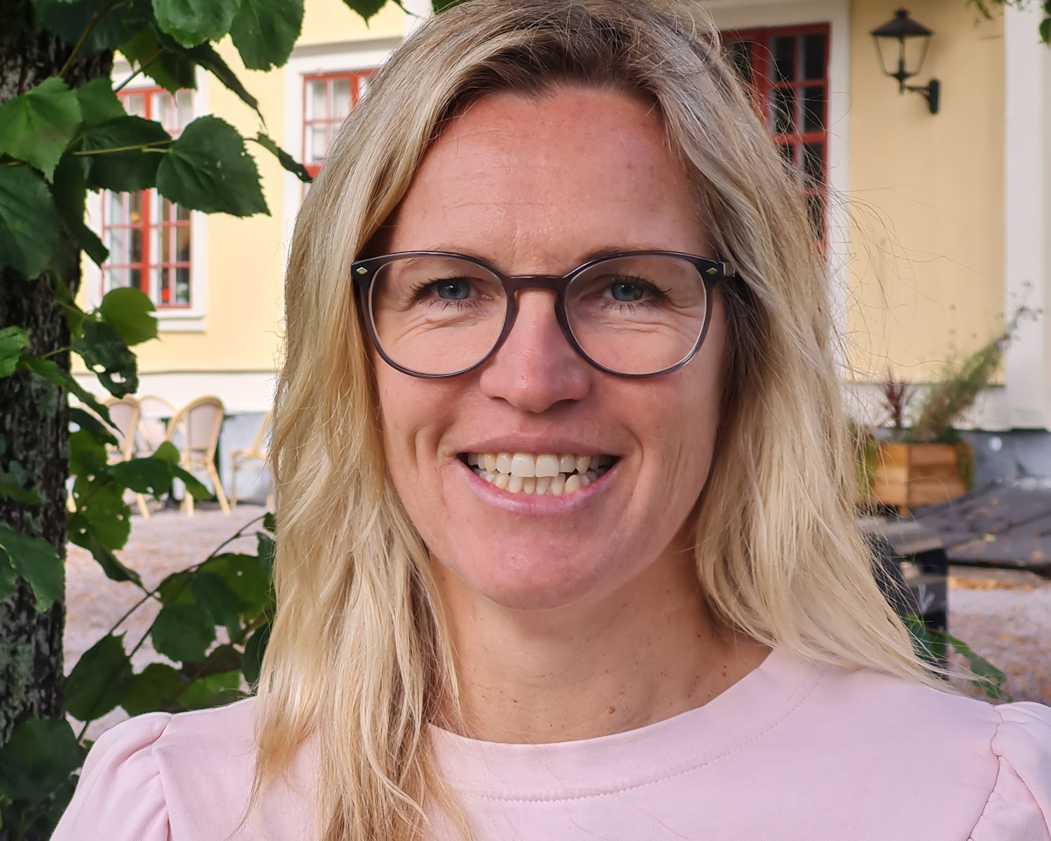 Porträttbild på blond kvinna med glasögon utomhus.