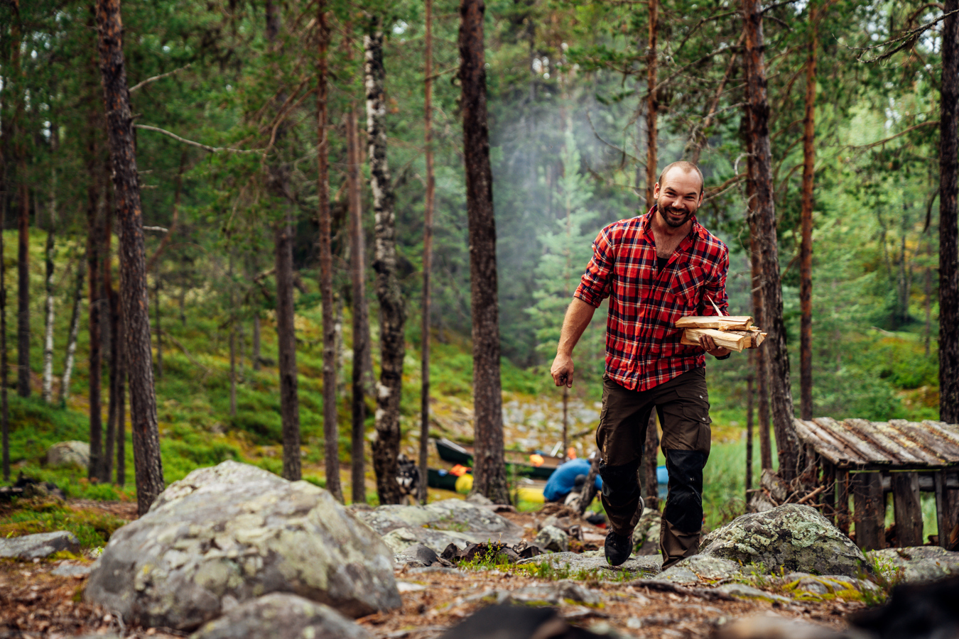 En man som bär på ved går genom tallskog