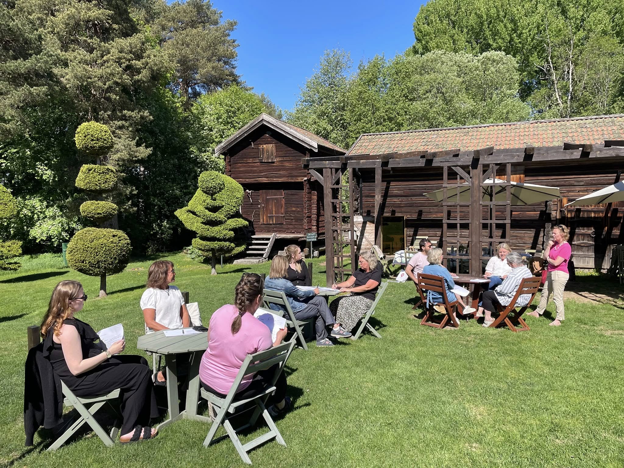 En grupp människor sitter i en trädgård sommartid.