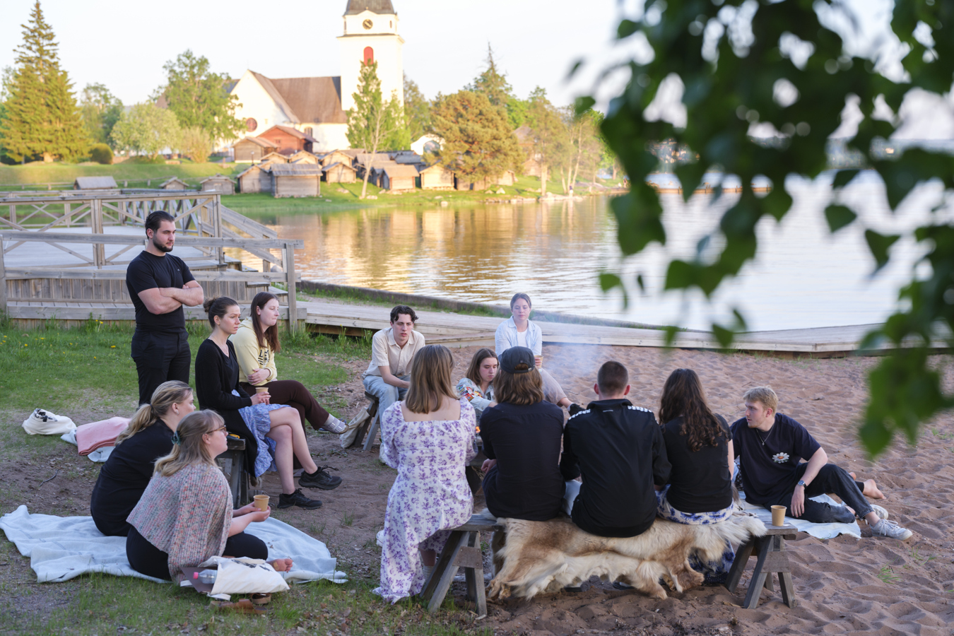 En grupp ungdomar runt en lägereld på en strand sommartid.