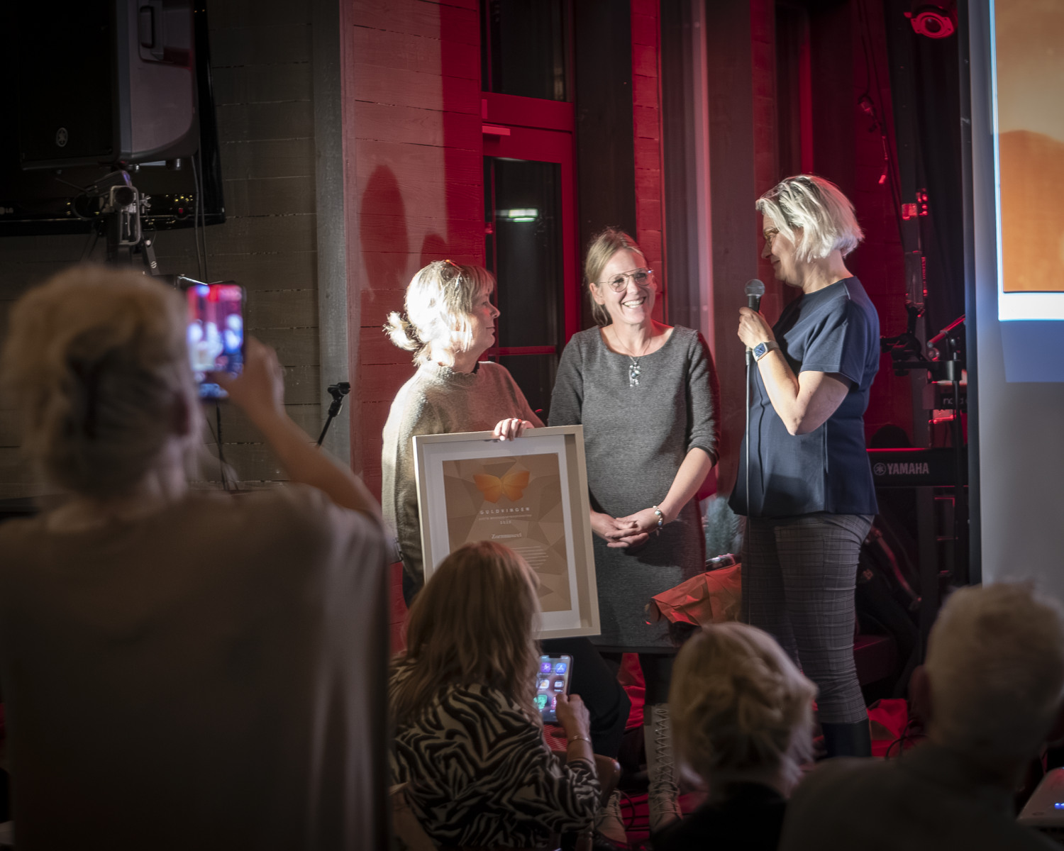 Tre kvinnor står på en scen under en prisutdelning.