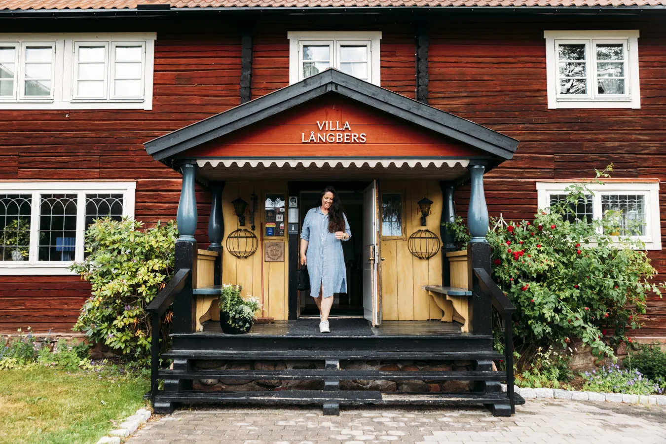 Kvinna går ut genom entré till ett falurött hus.