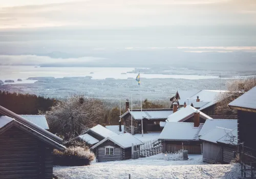 Äldre fäbodstugor vintertid med utsikt över sjö och snötäckt landskap.