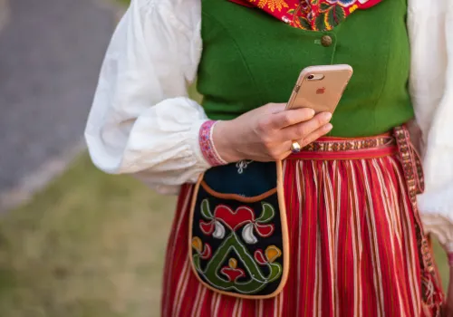 Kvinna iklädd folkdräkt håller i en mobil.
