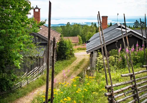 gärdsgård och fäbod i förgrunden med utsikt över sjö och skog,