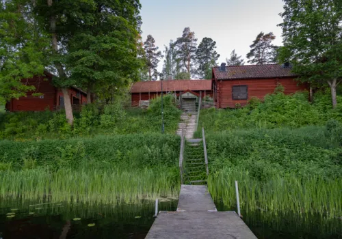Faluröd gårdslänga omgiven av grönska sommartid.