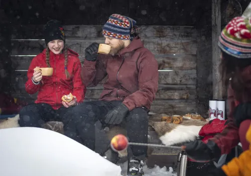 En familj sitter fikar utomhus vintertid.