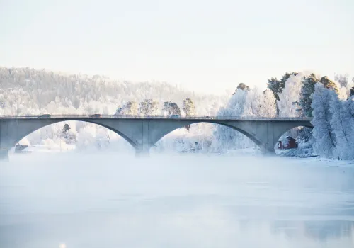 Bro med valv över dimmig älv vintertid.