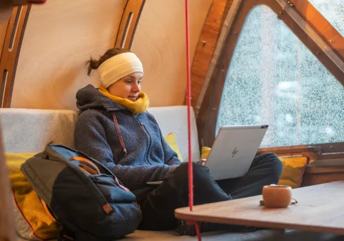 Kvinna sitter i skräddarställning med laptop i knät.