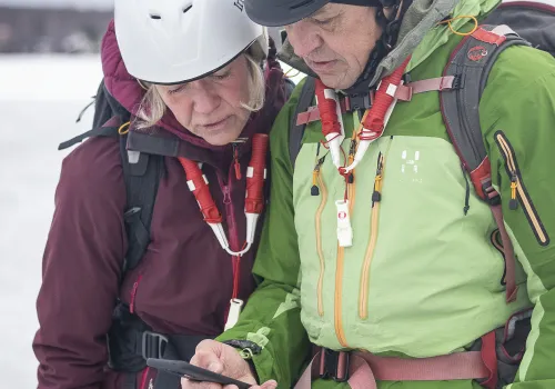 Två personer står på en is vintertid och tittar ner på en mobil.