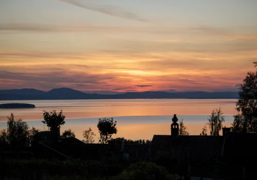 Solnedgång i rosa och orange med utsikt över sjö och berg.