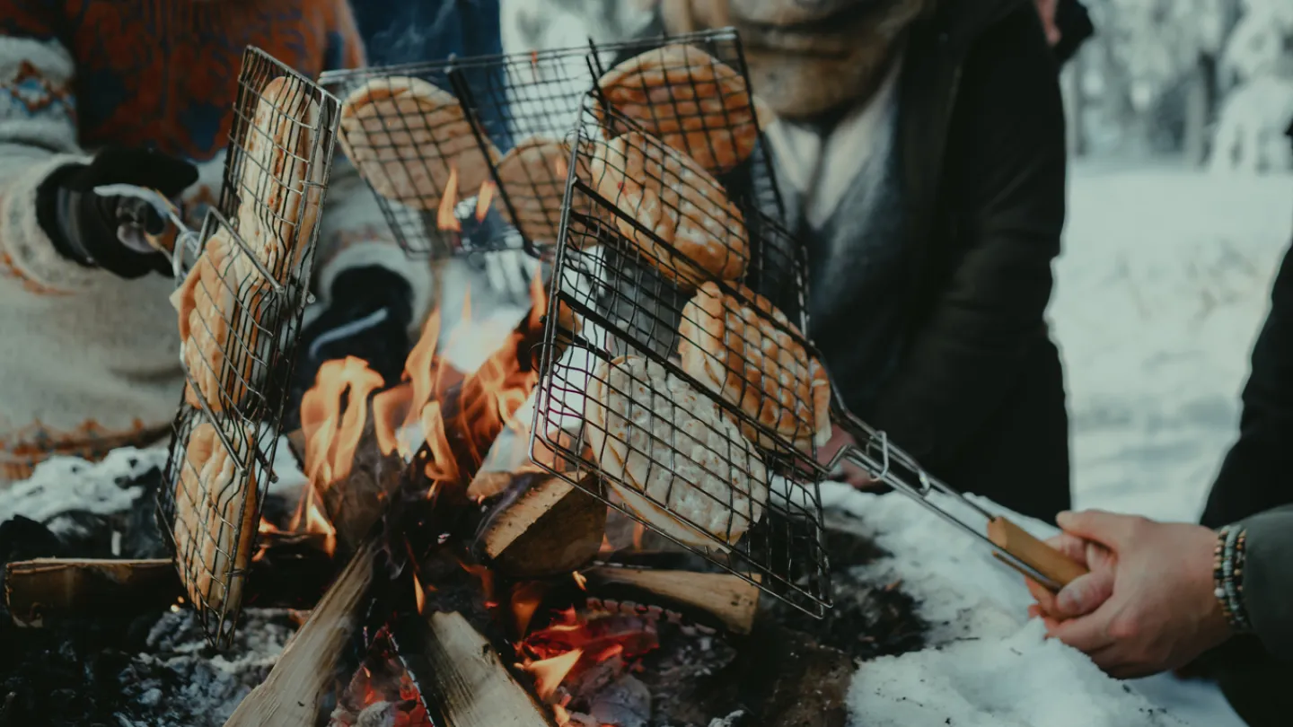 Flera personer grillar mackor över öppen eld vintertid.