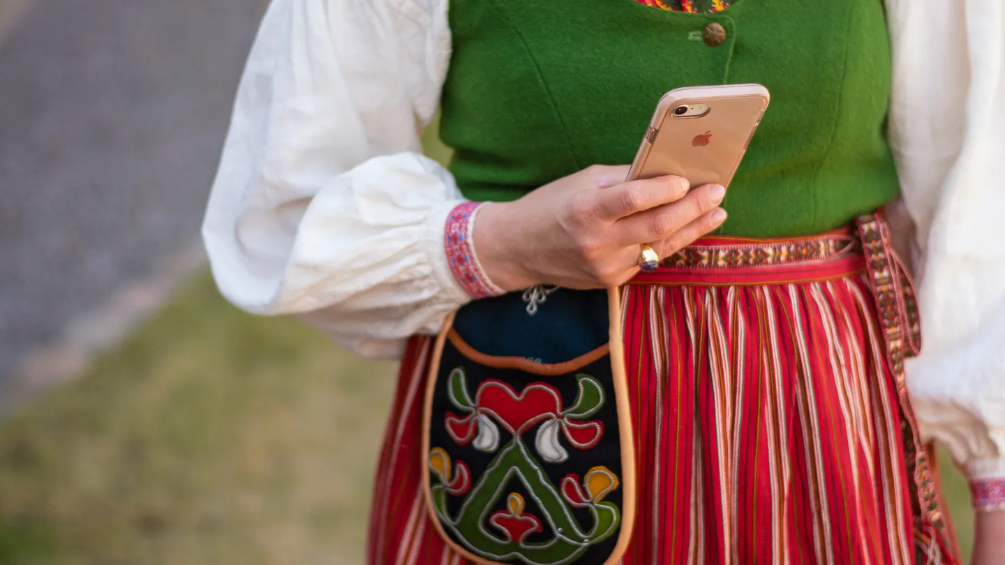 Kvinna iklädd folkdräkt håller i en mobil.