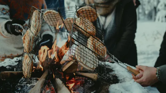 Flera personer grillar mackor över öppen eld vintertid.