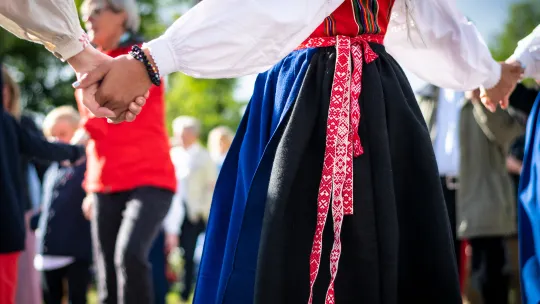 Närbild på person iklädd folkdräkt som dansar runt midsommarstång.