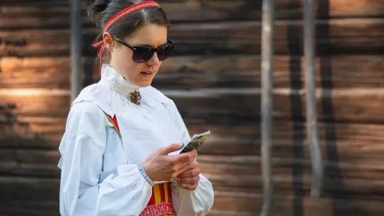 Kvinna i folkdräkt håller mobiltelefon.