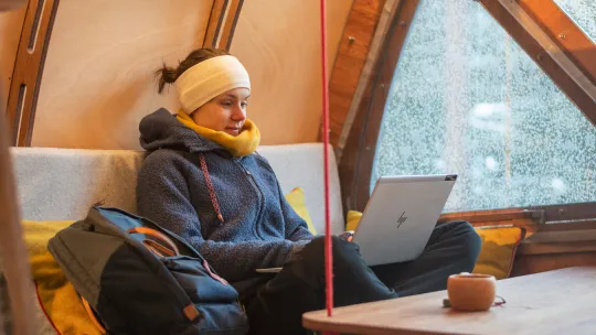Kvinna sitter i skräddarställning med laptop i knät.