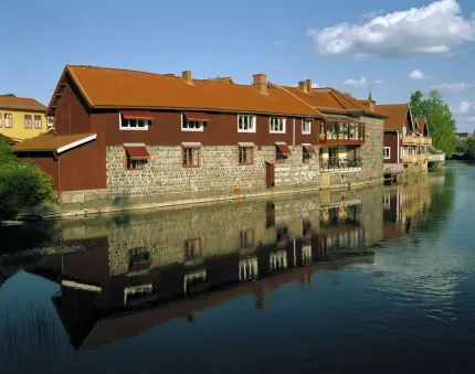 Older buildings in red wood and slag stone situated  by a river.