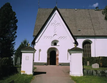Exteriörbild, två vita grindstolpar, kyrka i vit puts.