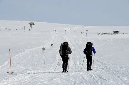 Två turskidåkare följer röda ledkryss på fjället.