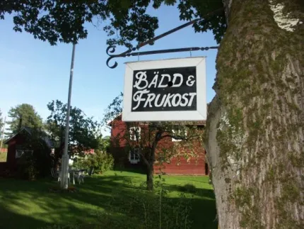 Skylt i ett träd framför gården med texten bädd och frukost.
