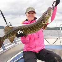 Glad tjej i cerise jacka visar stolt upp sin fångst av stor gädda.