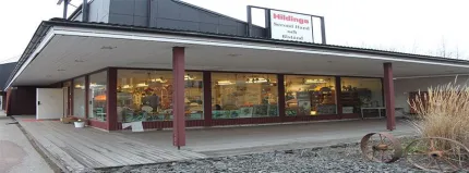 Byggnad med en rad med fönster, skylt Hildings second hand på taket, högre svart byggnad i bakrunden.