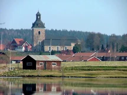 Vatten i förgrunden, tak och en tegelkyrka med svart tak i bakgrunden.