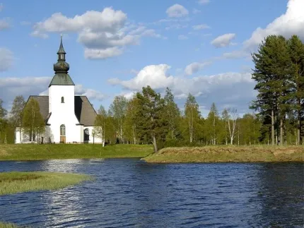Exterior white church with streams in front and greenery around.
