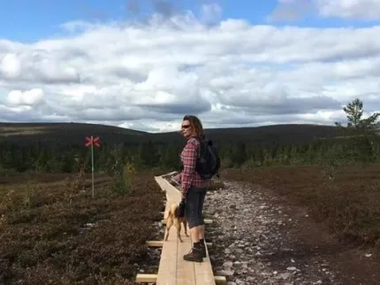 En person med hund vandrar på en spång i fjällmiljö.