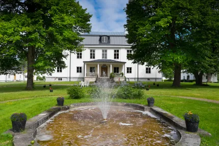 Fontän med vit herrgård i bakgrunden sommartid.